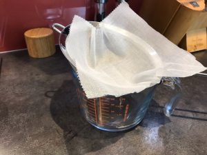 Muslin cloth lining a sieve over a glass jug.